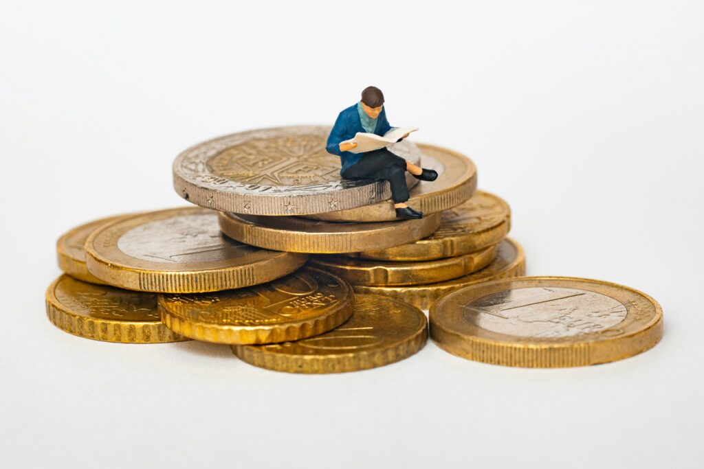 Homem em miniatura sentado sobre moedas aprendendo sobre como criar reserva de emergência.