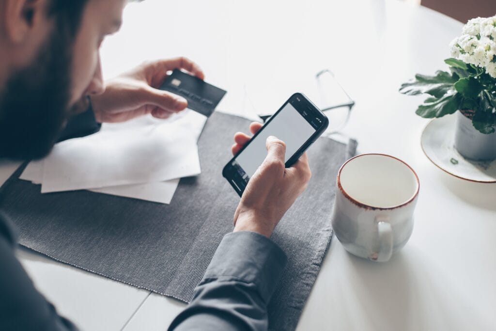 Pessoa utilizando cartão de crédito e celular para entender como funciona o rotativo do cartão.