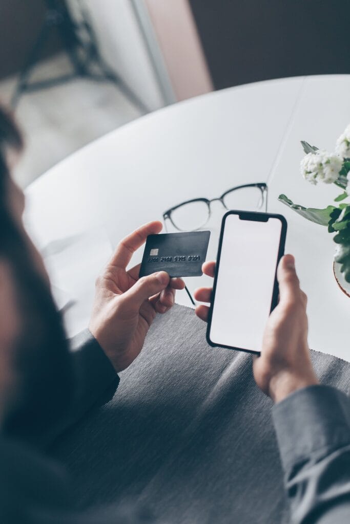 Pessoa segurando um cartão de crédito e um smartphone enquanto consulta informações sobre o rotativo do cartão.