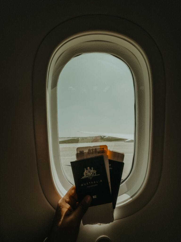 Passaporte e cartão de embarque na janela de um avião representando formas inteligentes de acumular milhas para viajar.