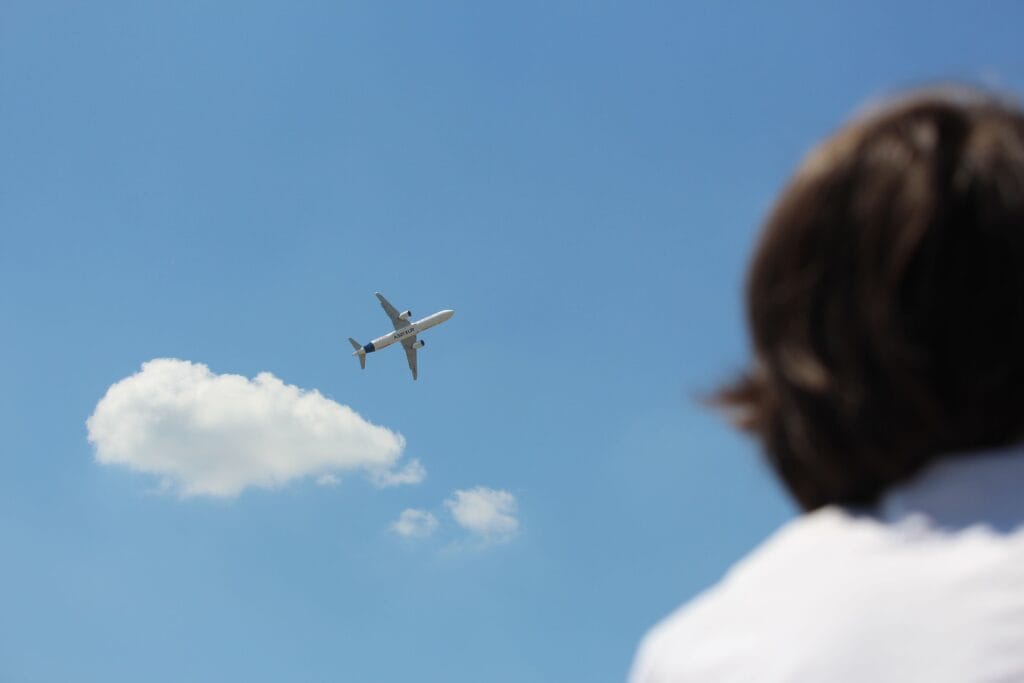 Pessoa observando um avião no céu, representando o objetivo de acumular milhas para viajar pagando menos.