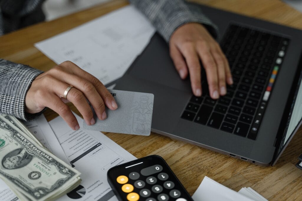 Pessoa utilizando cartão de crédito, calculadora e notebook para organizar gastos e controlar as finanças pessoais.